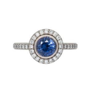 Bague Or Blanc avec Saphir Bleu entouré de diamants. Le corps de la bague contient également des diamants.