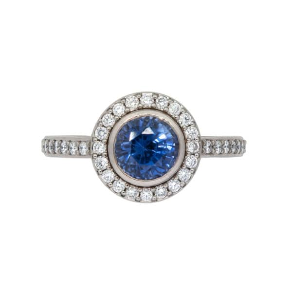 Bague Or Blanc avec Saphir Bleu entouré de diamants. Le corps de la bague contient également des diamants.